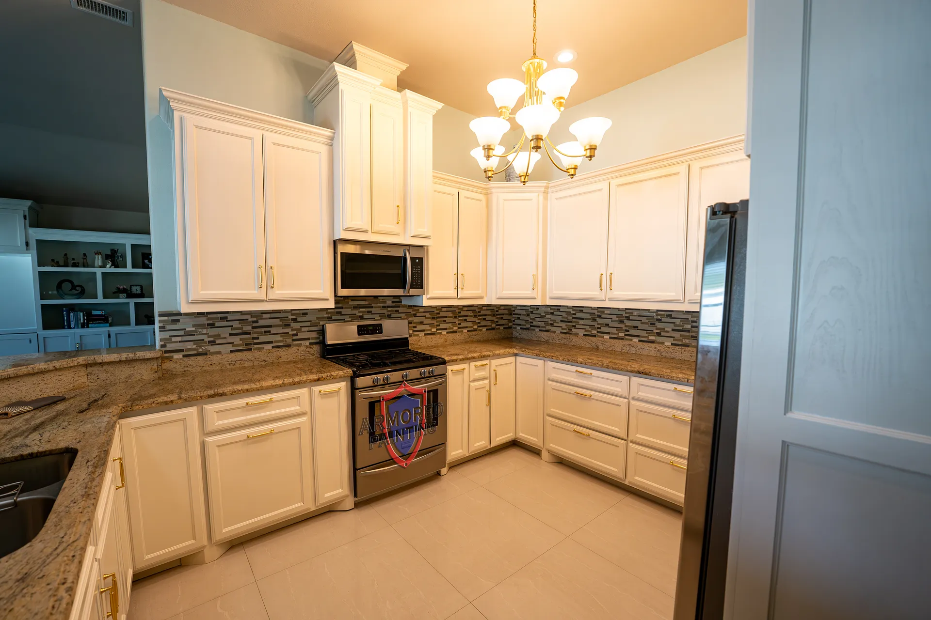 Cream refinished kitchen cabinets with granite counters and a chandelier