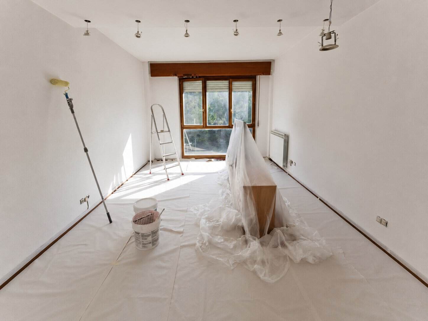 The same living room being repainted bright white, furniture covered