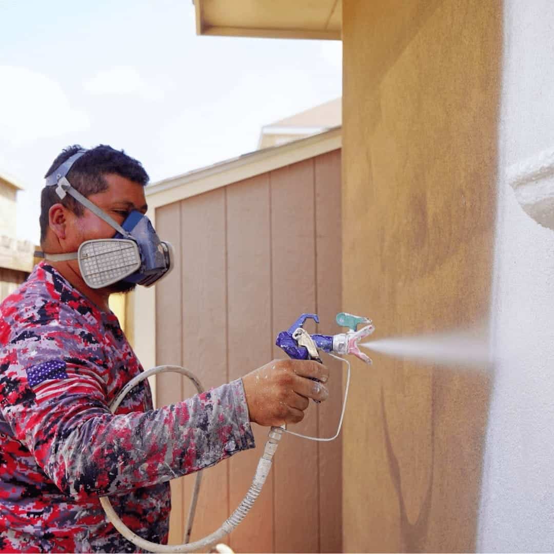 Painter in a respirator spraying an exterior stucco wall