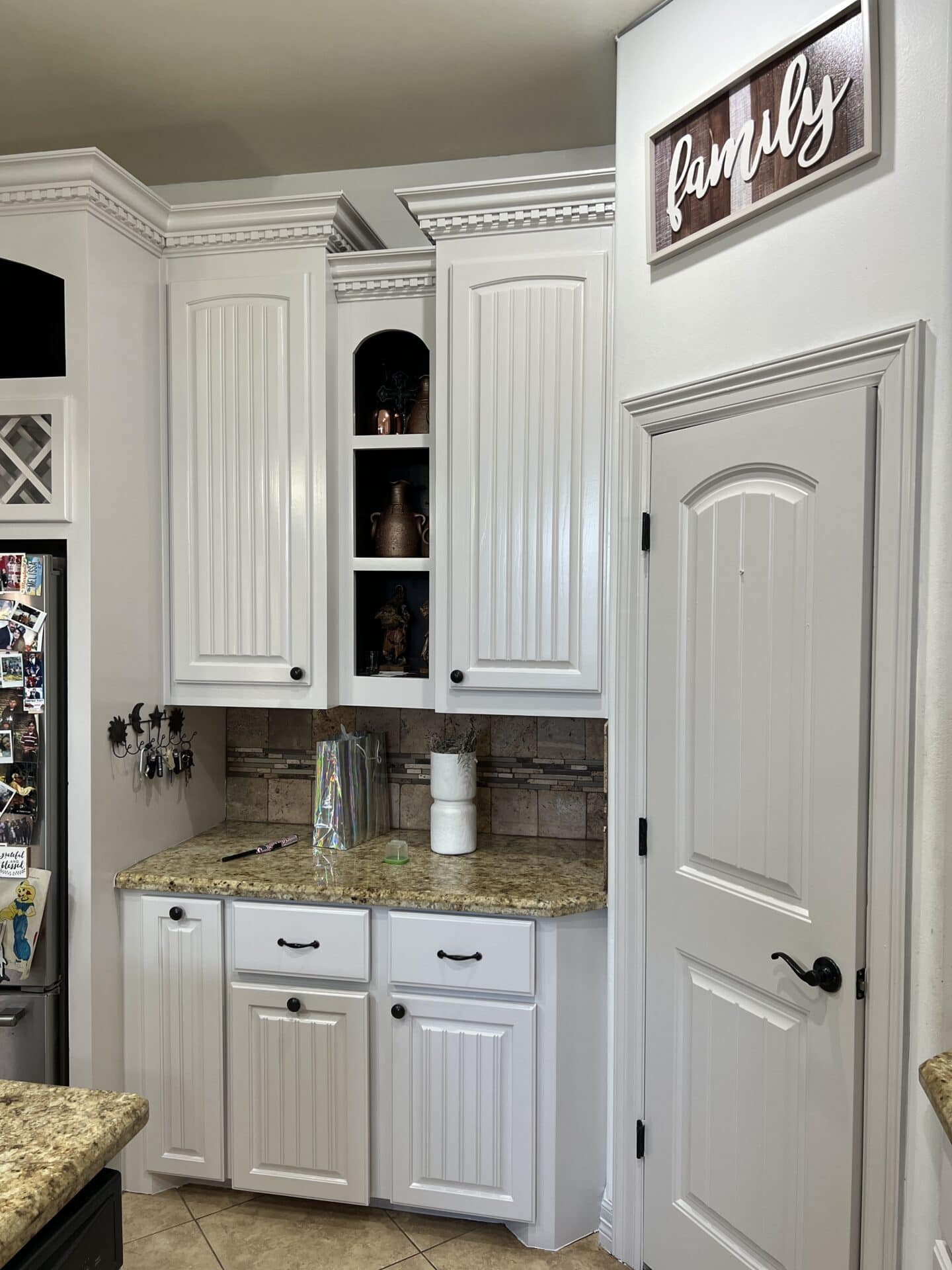 Neat kitchen corner with white cabinetry, granite countertops, and a tiled backsplash. "Family" sign above, creating a warm, welcoming atmosphere.