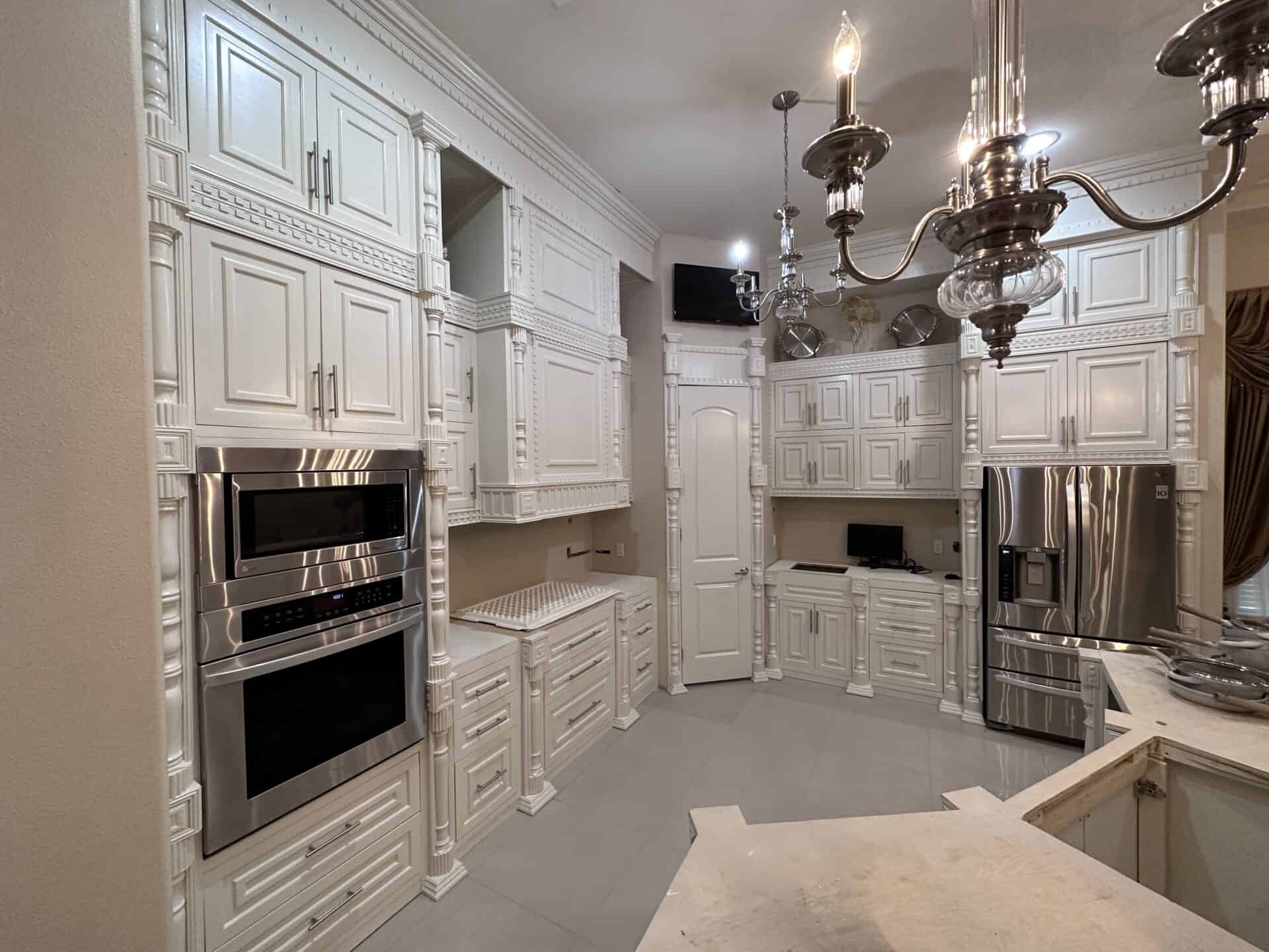 Elegant kitchen with ornate white cabinetry, stainless steel appliances, and a glossy chandelier. The space feels luxurious and polished.