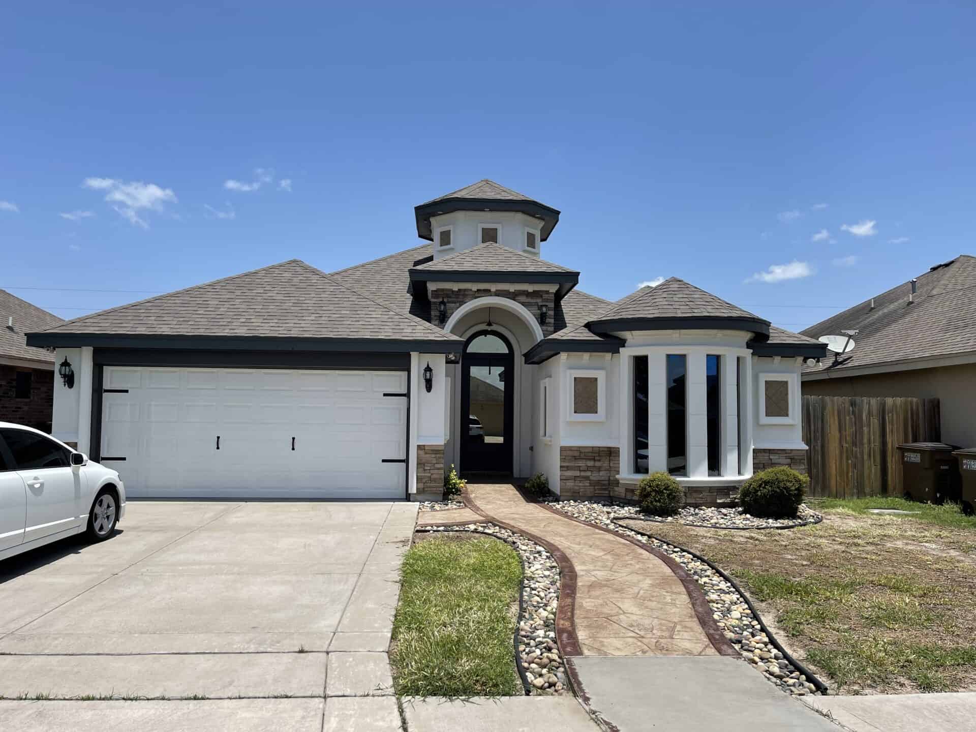 Single-story house with a turret and arched entrance. Features include a large garage, curved pathway, and bay windows. Clear skies convey a tranquil mood.