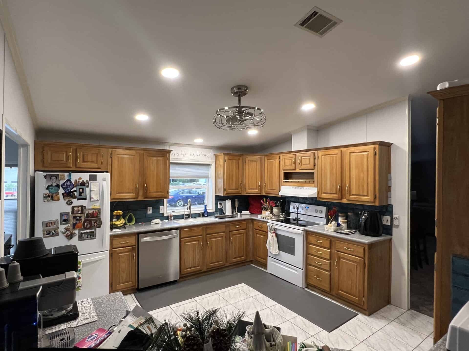 Warm kitchen with wooden cabinets, white appliances, and a gray countertop. Fridge is covered with photos. Soft lighting gives a cozy feel.