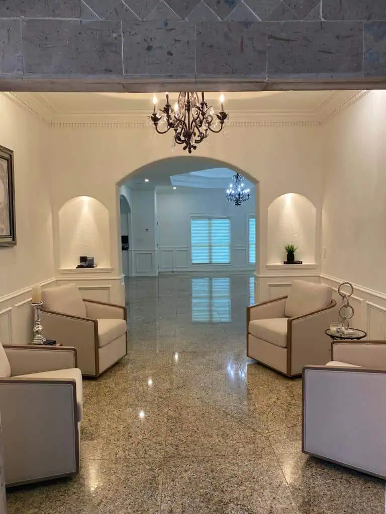 Elegant lounge with four beige armchairs set on glossy stone floor, beneath a vintage chandelier. Soft lighting and decorative plants create a cozy ambiance.